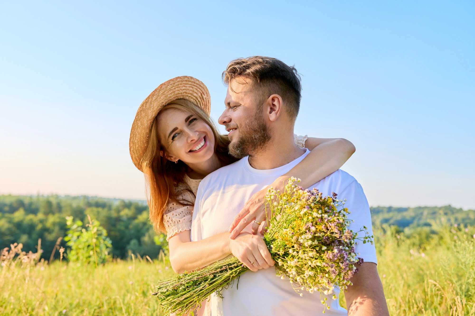 Happy middle-aged couple in love embracing, with a bouquet of wildflowers,